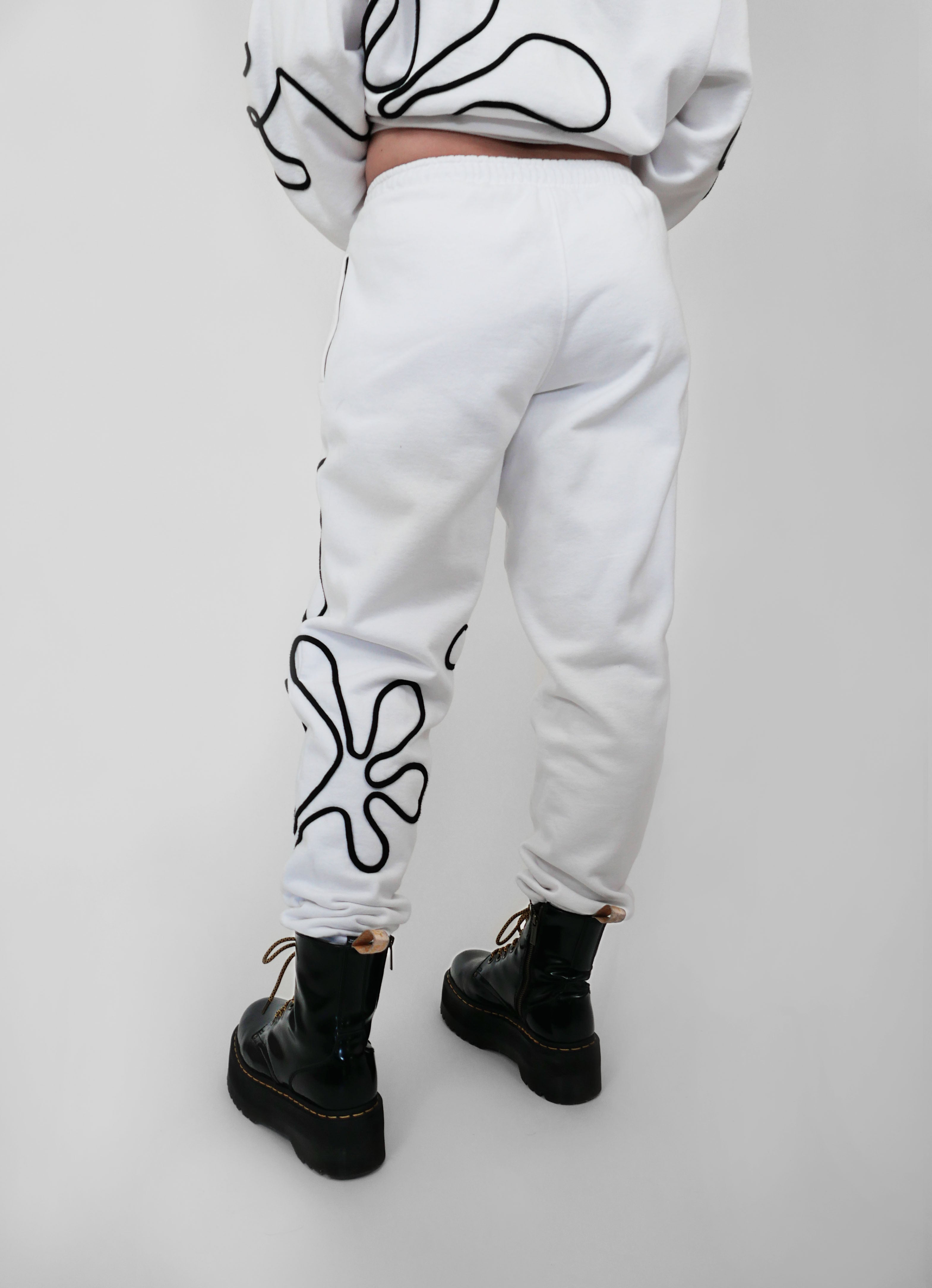 White sweatpants with black abstract one-line designs worn by a person on a light gray background