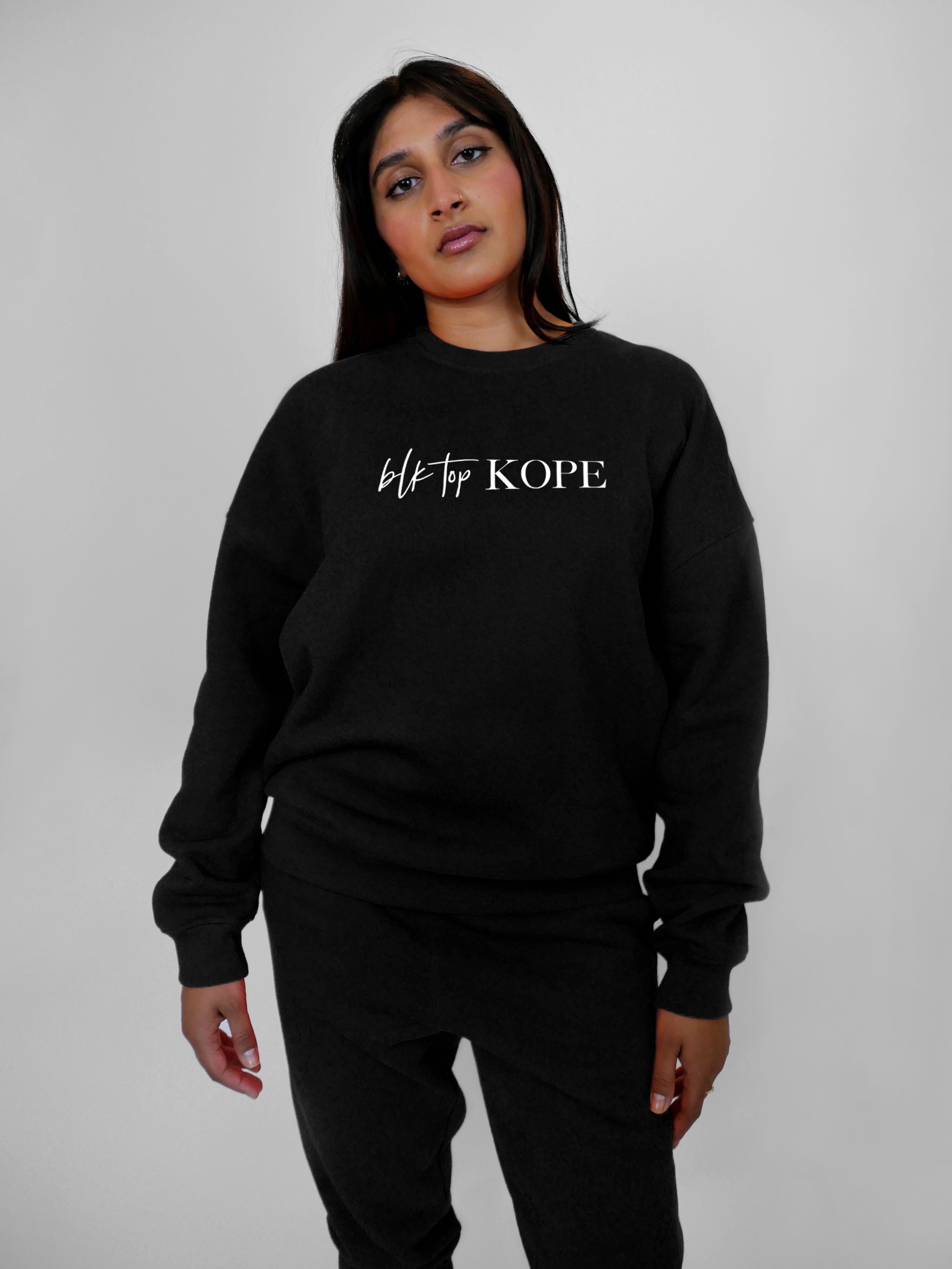 Person wearing a black crewneck with 'blk top Kope' text on a plain background