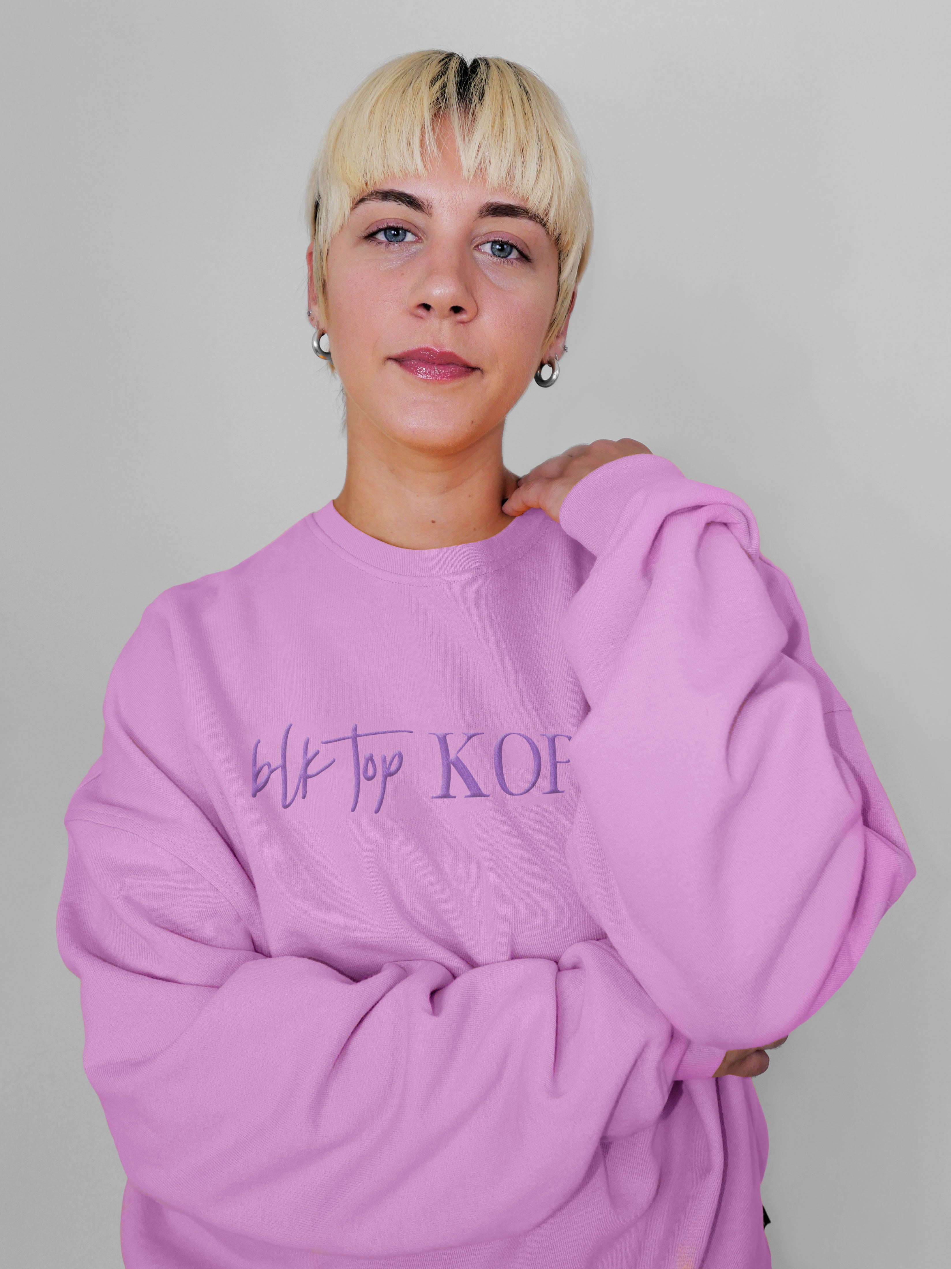Person wearing a blush crewneck with text on it against a plain background