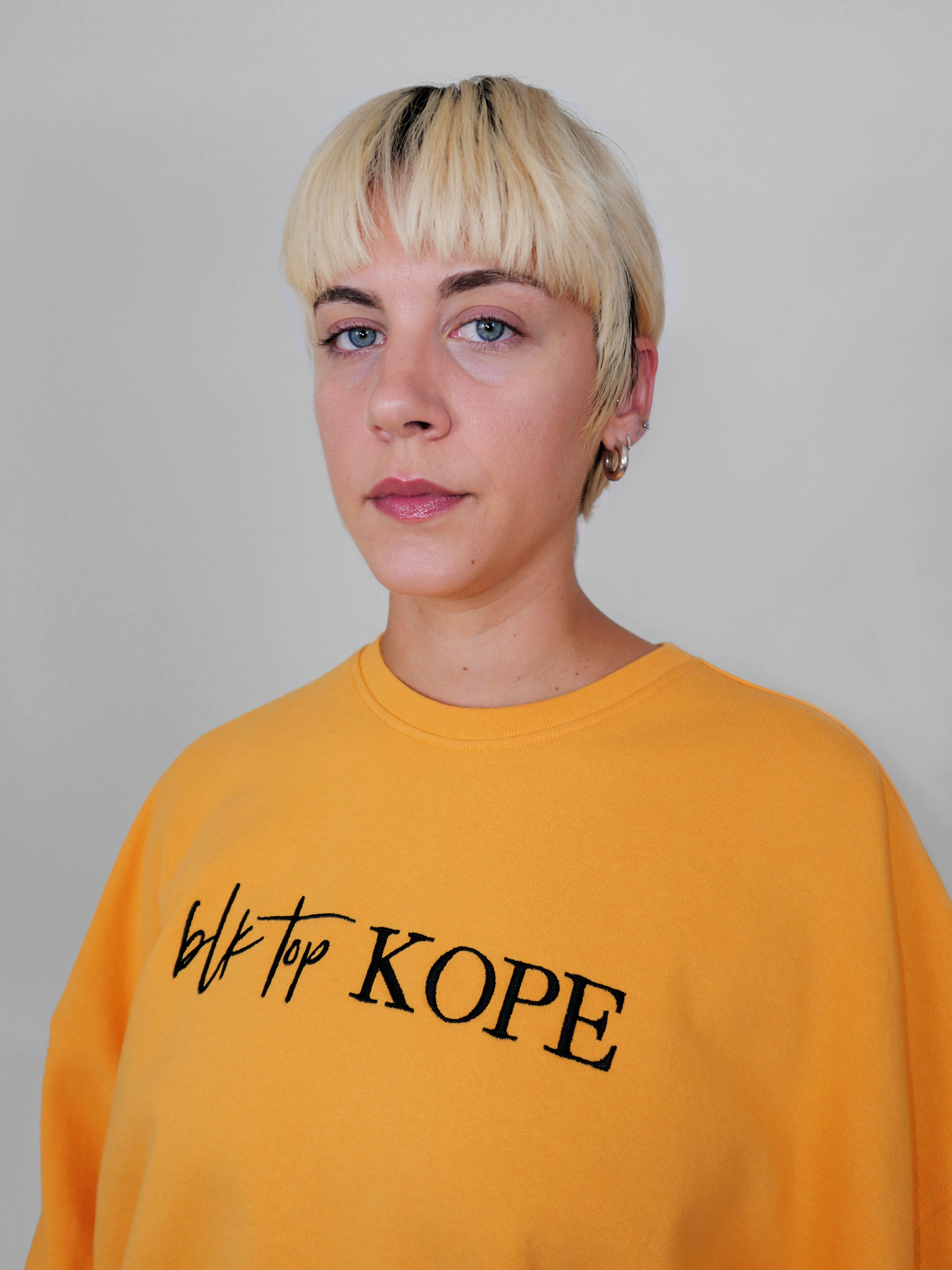 Person wearing a yellow crewneck with 'blk top Kope' text on a plain background