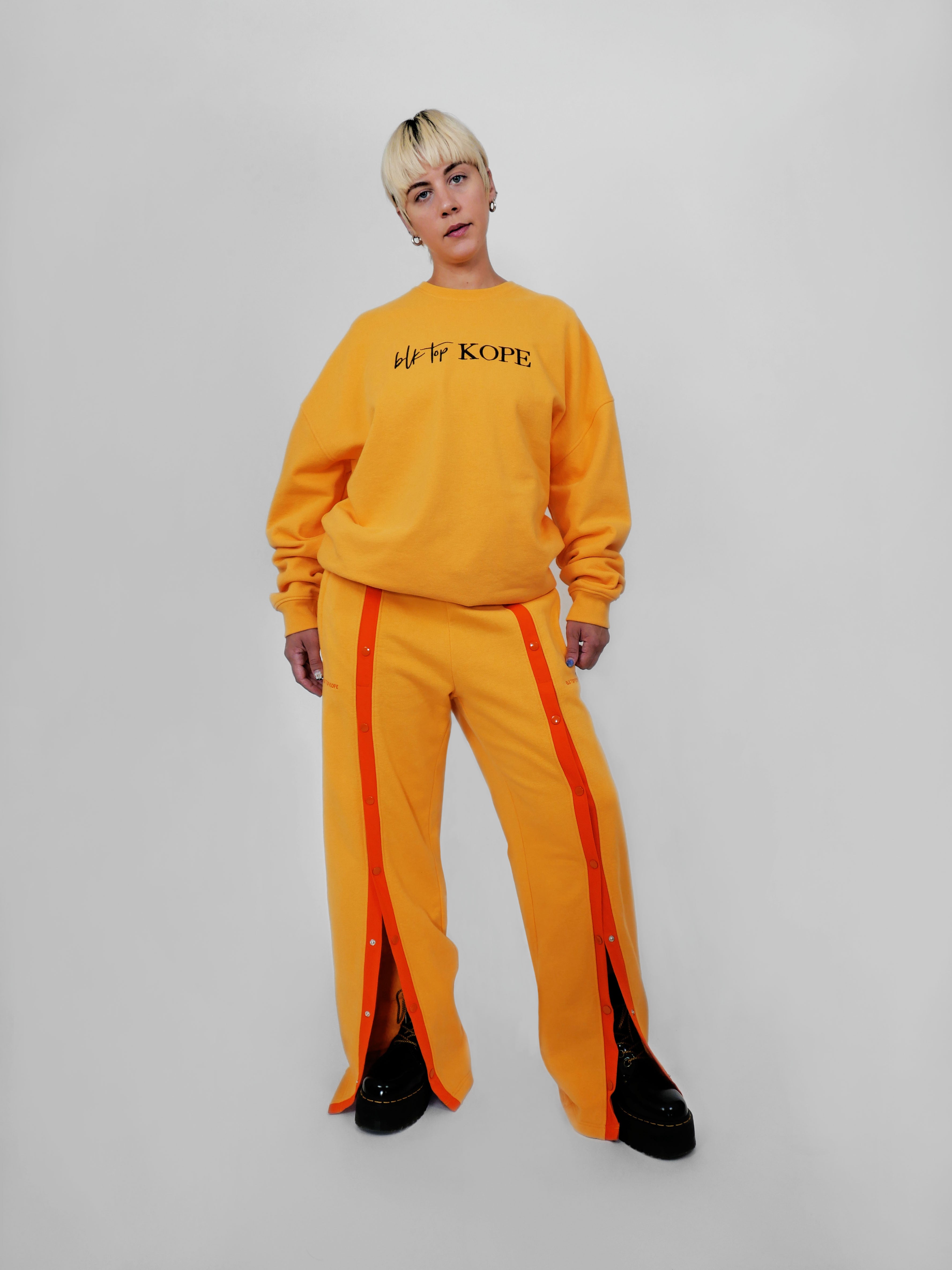 Person wearing a yellow tracksuit with orange stripes on a plain background