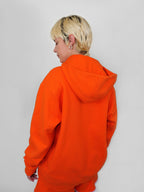 Person wearing an orange hoodie and pants on a plain background