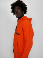 Person wearing an orange hoodie with a brand logo on a white background
