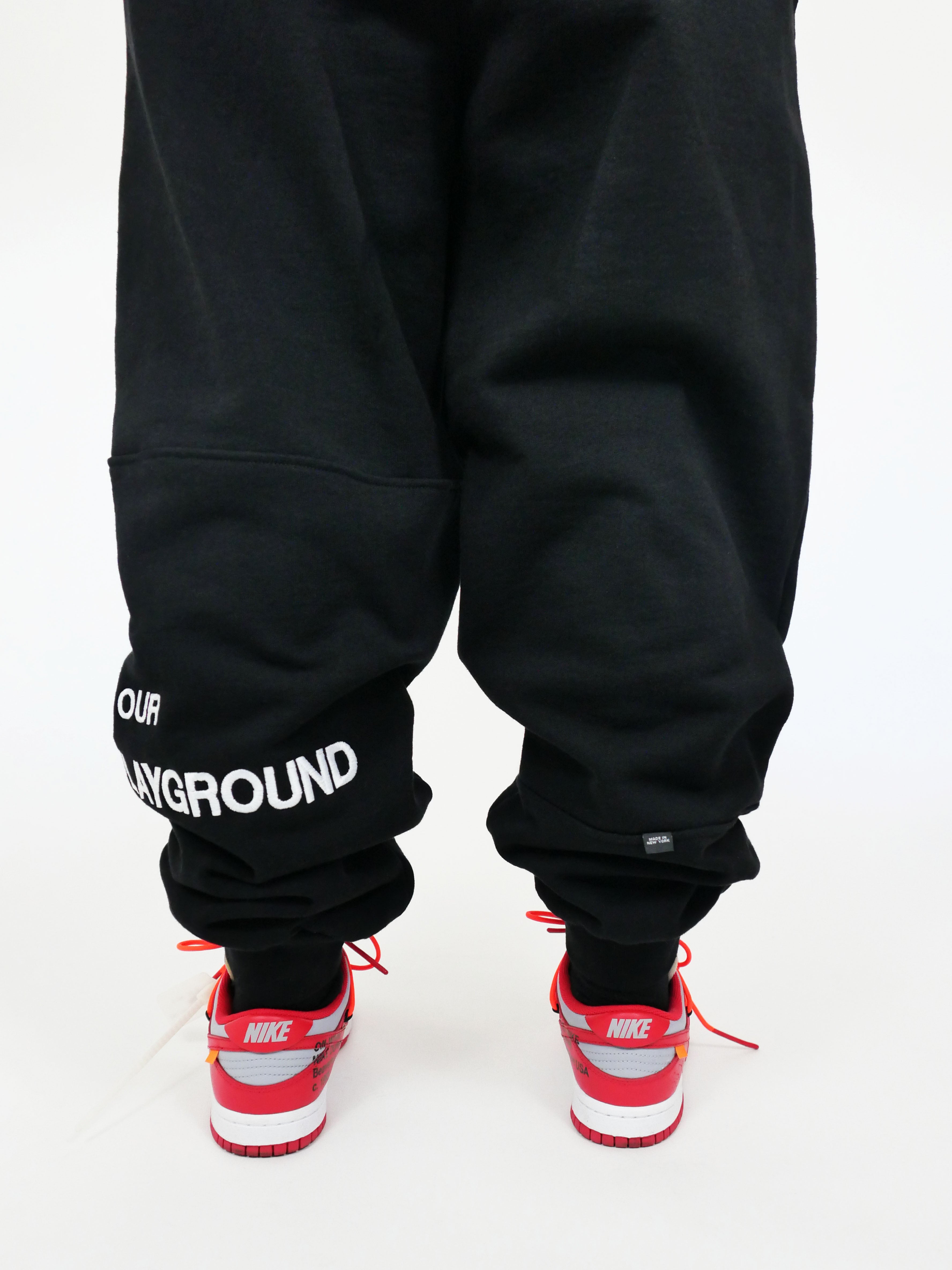 Black sweatpants with visible branding and red Nike sneakers on a white background