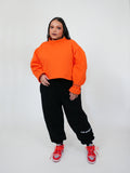 Person wearing an orange sweatshirt and black sweatpants with red shoes on a white background