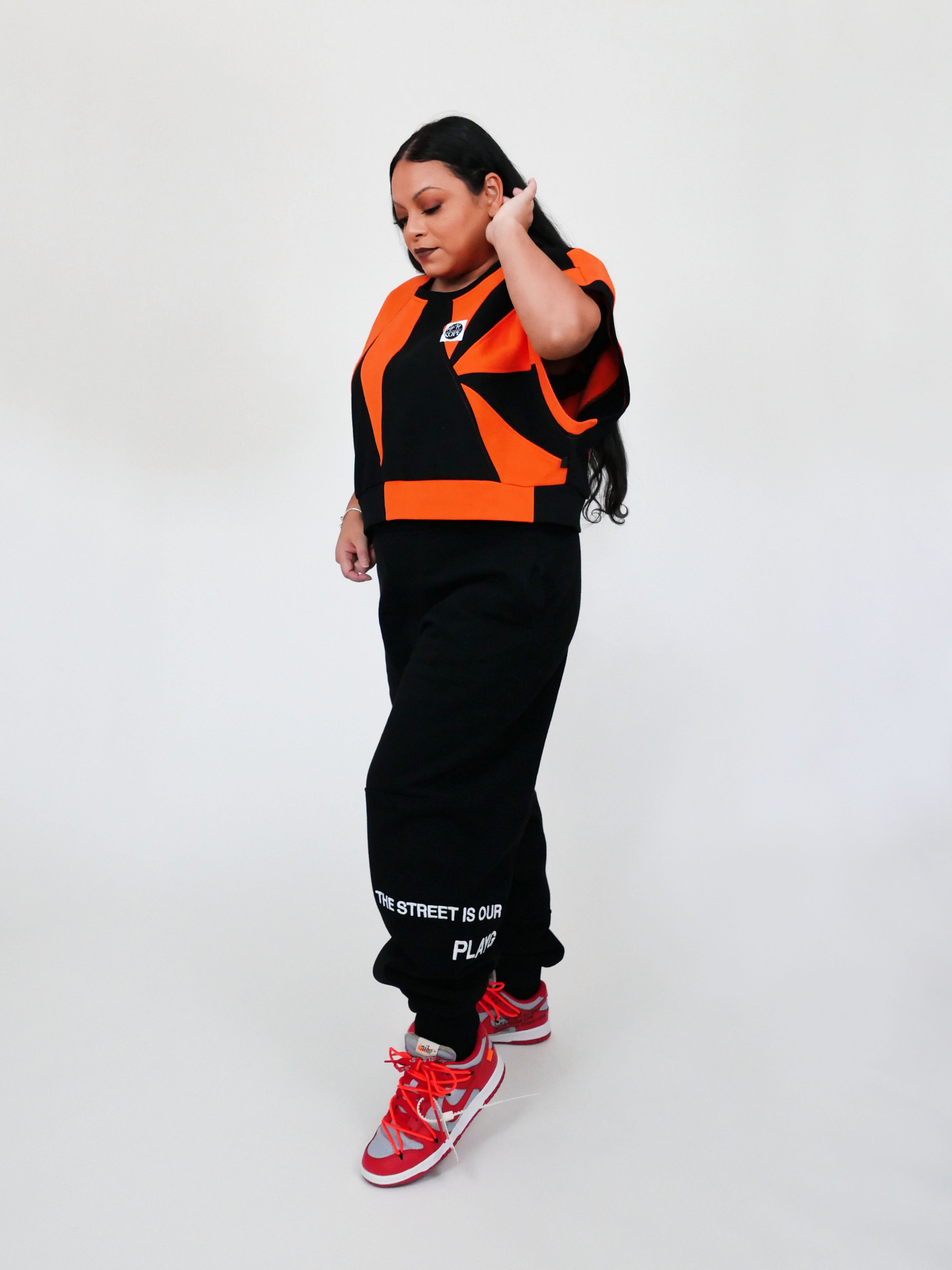 Person wearing an orange and black outfit with red sneakers on a white background