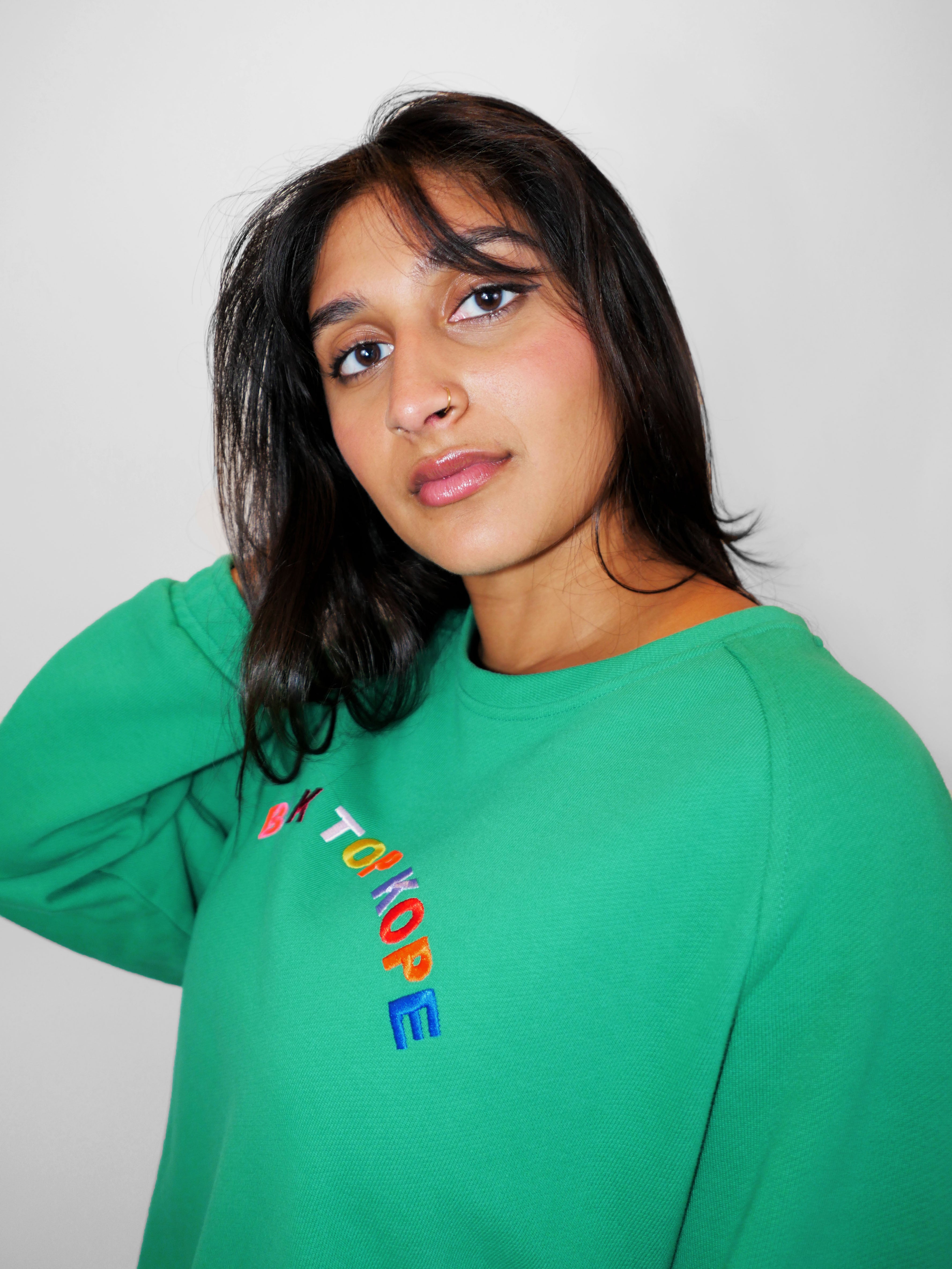 Woman wearing a green crewneck with colorful text on a plain background