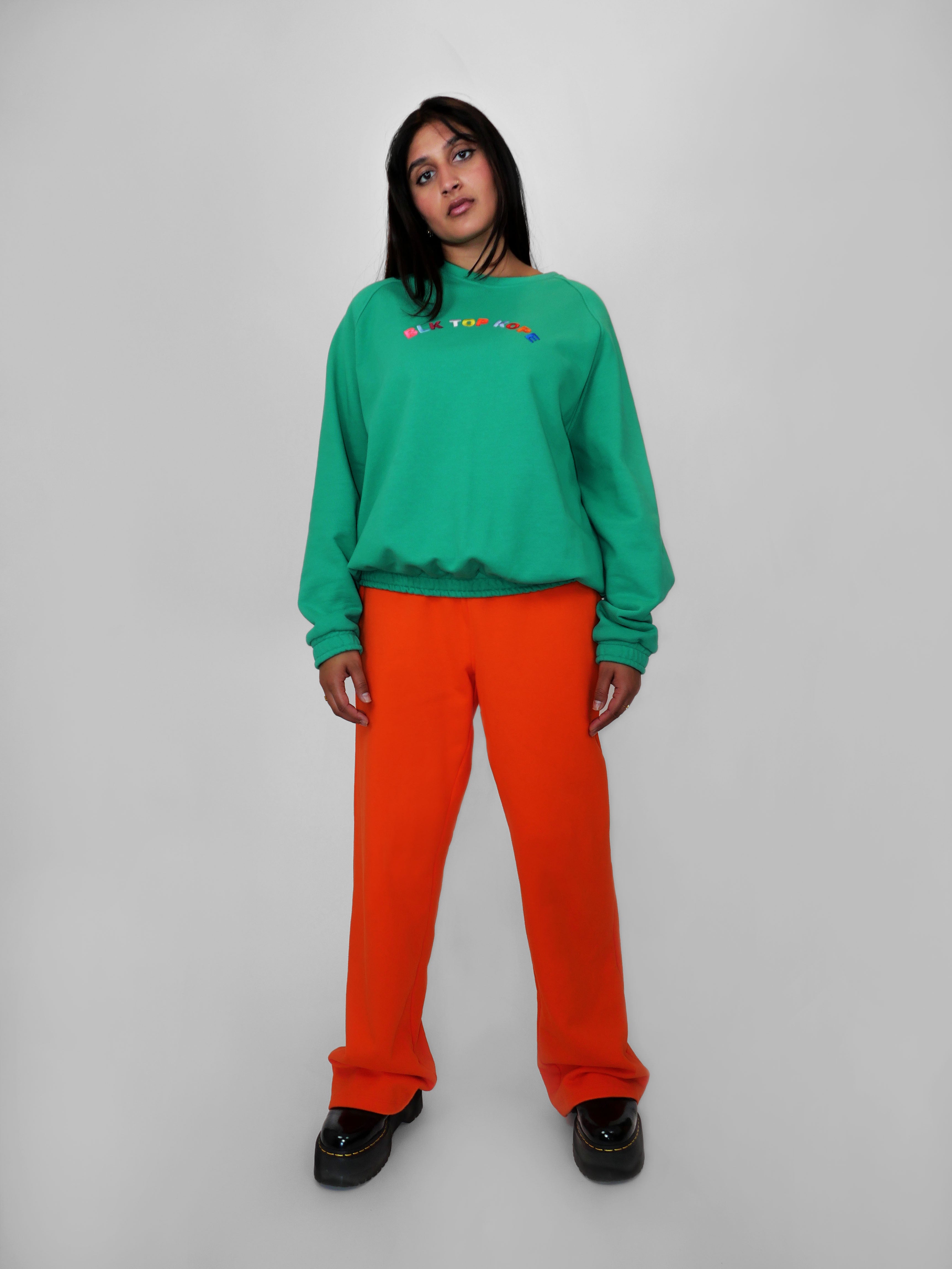 Woman wearing a green crewneck and orange pants on a white background