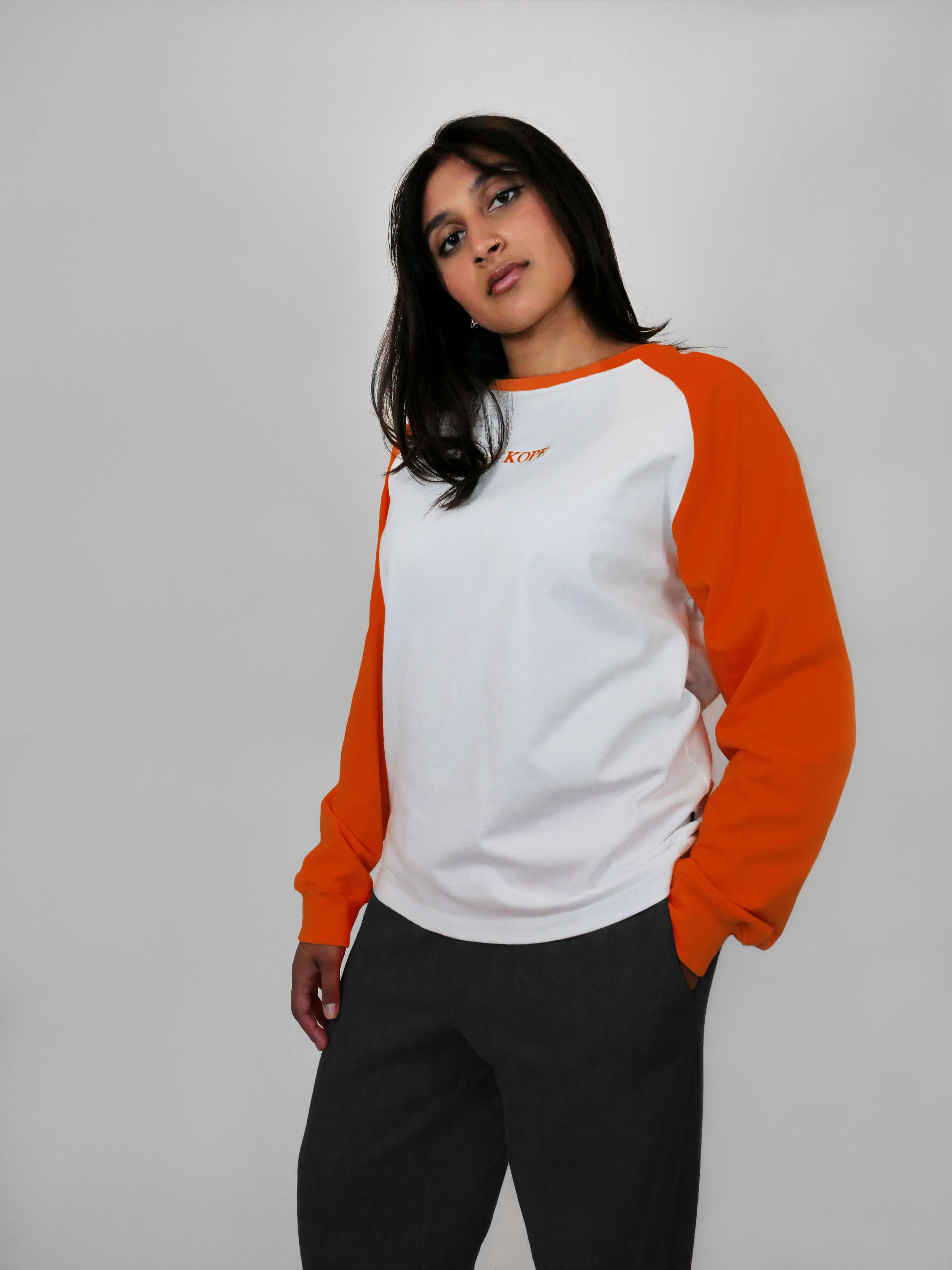 Woman wearing an orange and white raglan longsleeve on a plain background