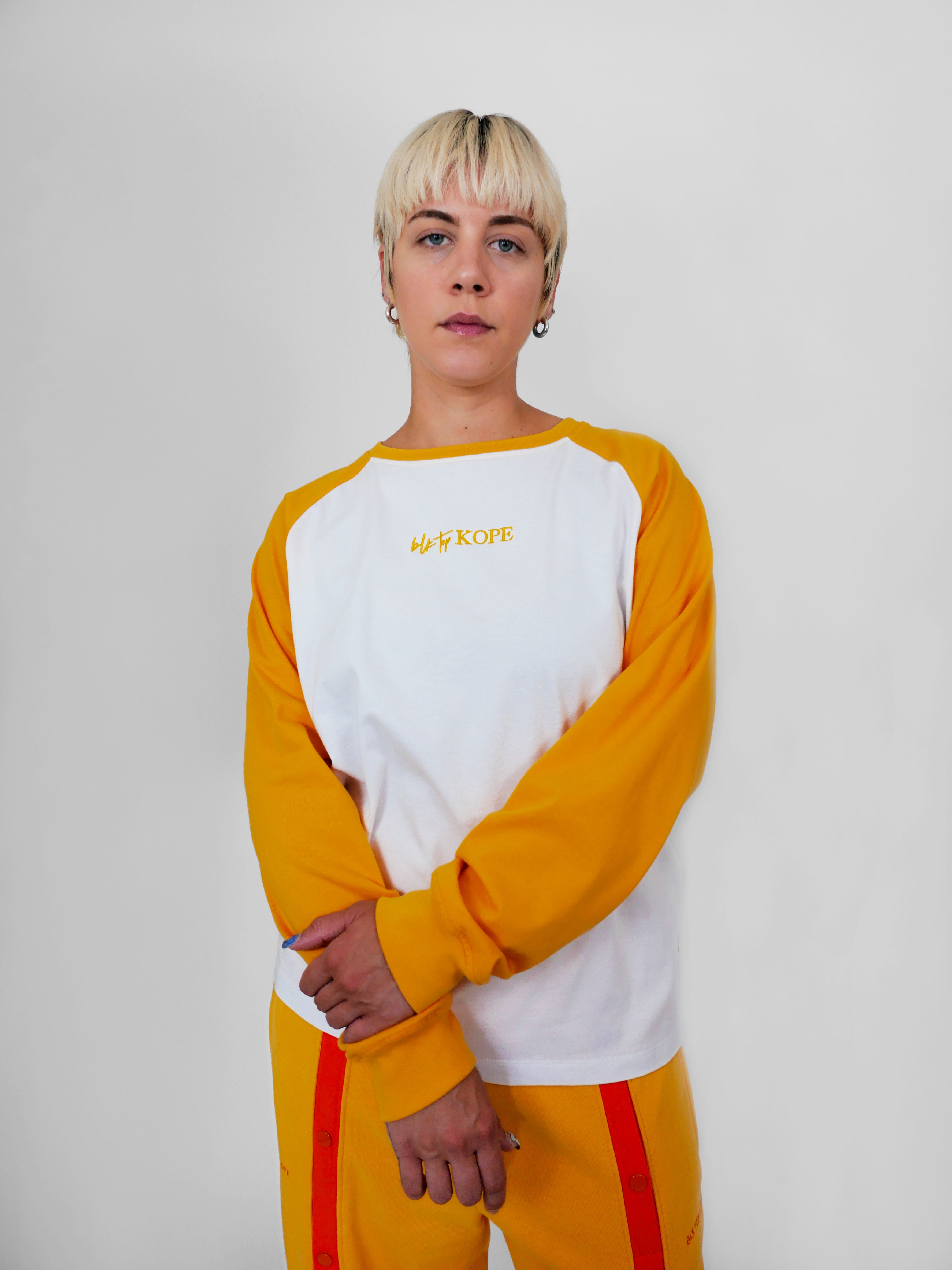 Woman wearing a yellow and white raglan longsleeve  on a plain background