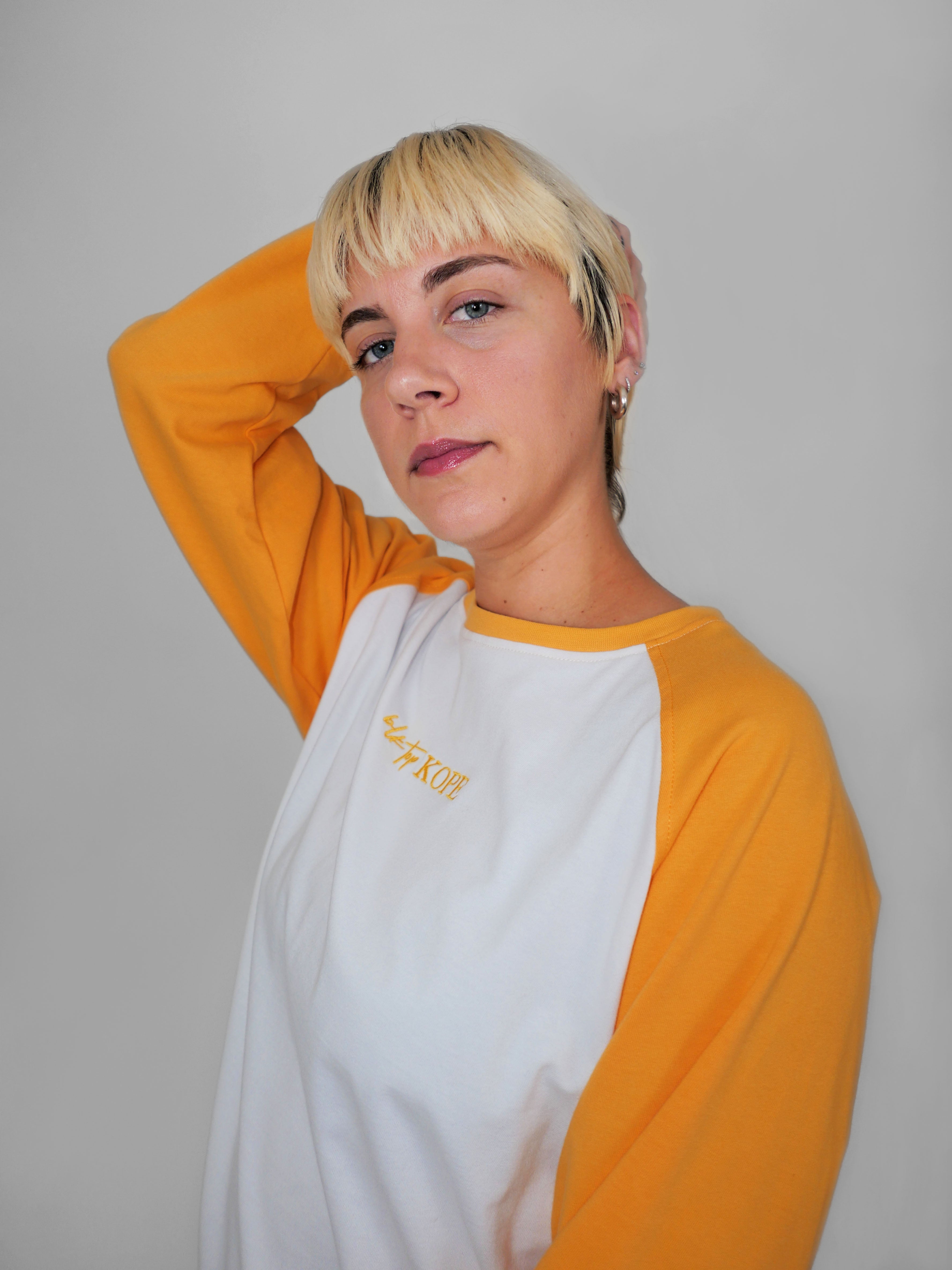 Woman wearing a yellow and white raglan longsleeve with a logo on a plain background