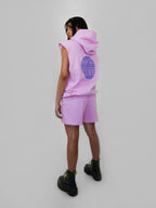 Person wearing a blush sleeveless hoodie and shorts set with a visible brand logo on a light gray background