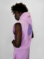 Person wearing a blush sleeveless hoodie with a brand logo on a white background
