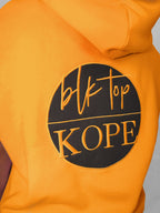 Yellow sleeveless hoodie with 'blk top Kope' logo on a gray background