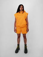 Person wearing a yellow sleeveless hoodie and shorts set with black boots on a white background