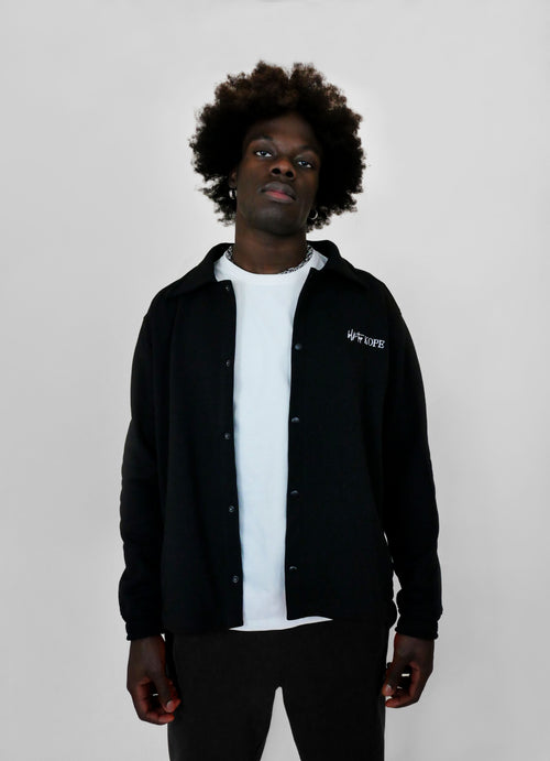 Person wearing a black snap jacket with a brand logo on a plain background