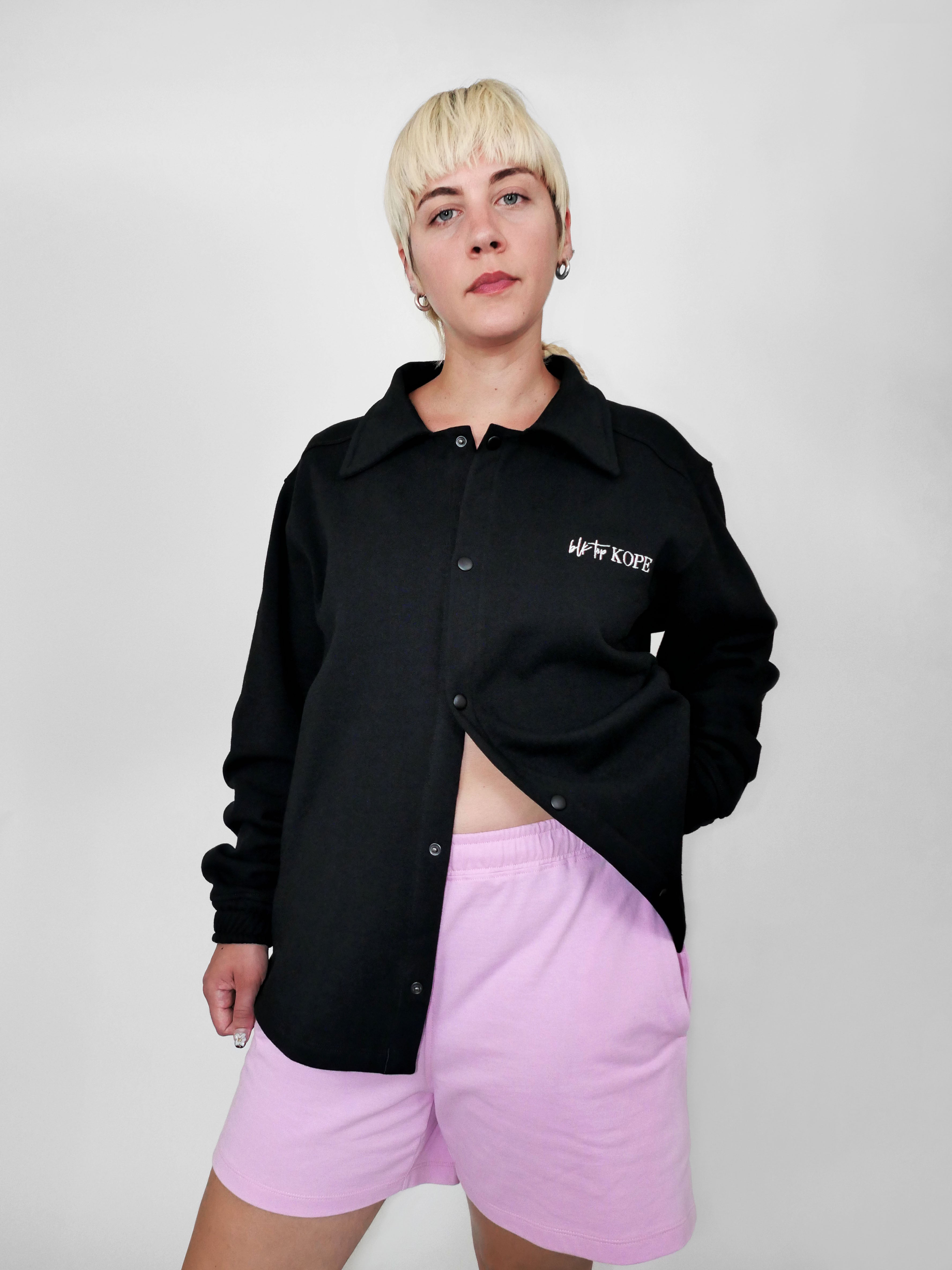 Person wearing a black snap jacket with text and pink shorts on a white background