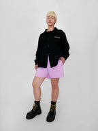 Person wearing a black snap jacket, pink shorts, and black boots on a white background