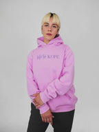 Person wearing a blush hoodie with text on a plain background