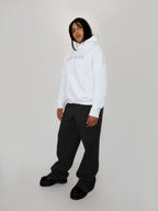 Person wearing a white hoodie and black sweatpants on a plain background