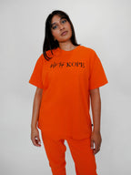 Person wearing an orange outfit with 'blk top KOPE' text on a plain background