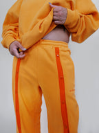 Person wearing yellow snap sweatpants with an orange front stripe on a plain background