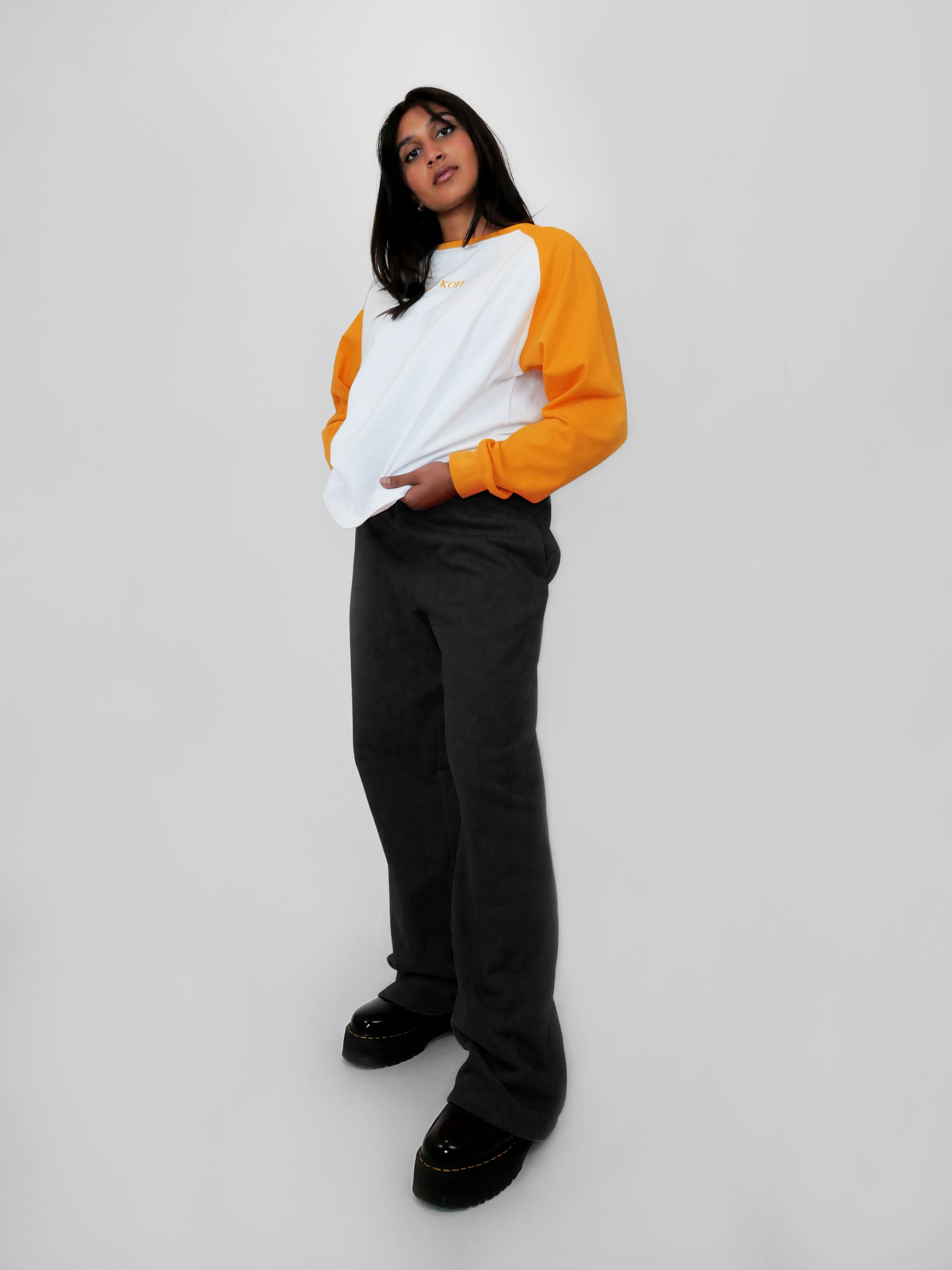Person wearing a raglan longsleeve with yellow sleeves and black straight leg sweatpants on a plain background