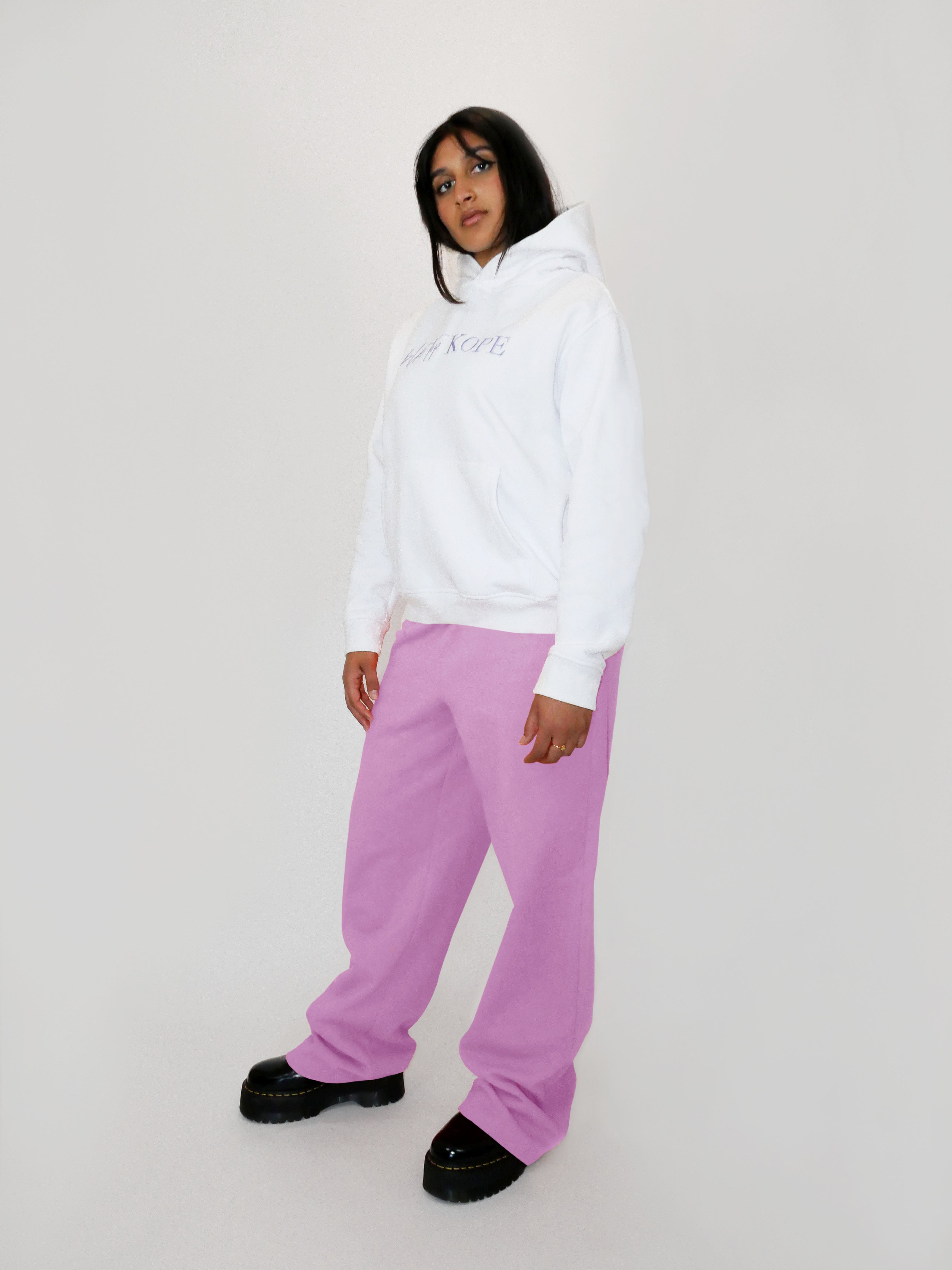 Person wearing a white hoodie and blush straight leg sweatpants on a plain background