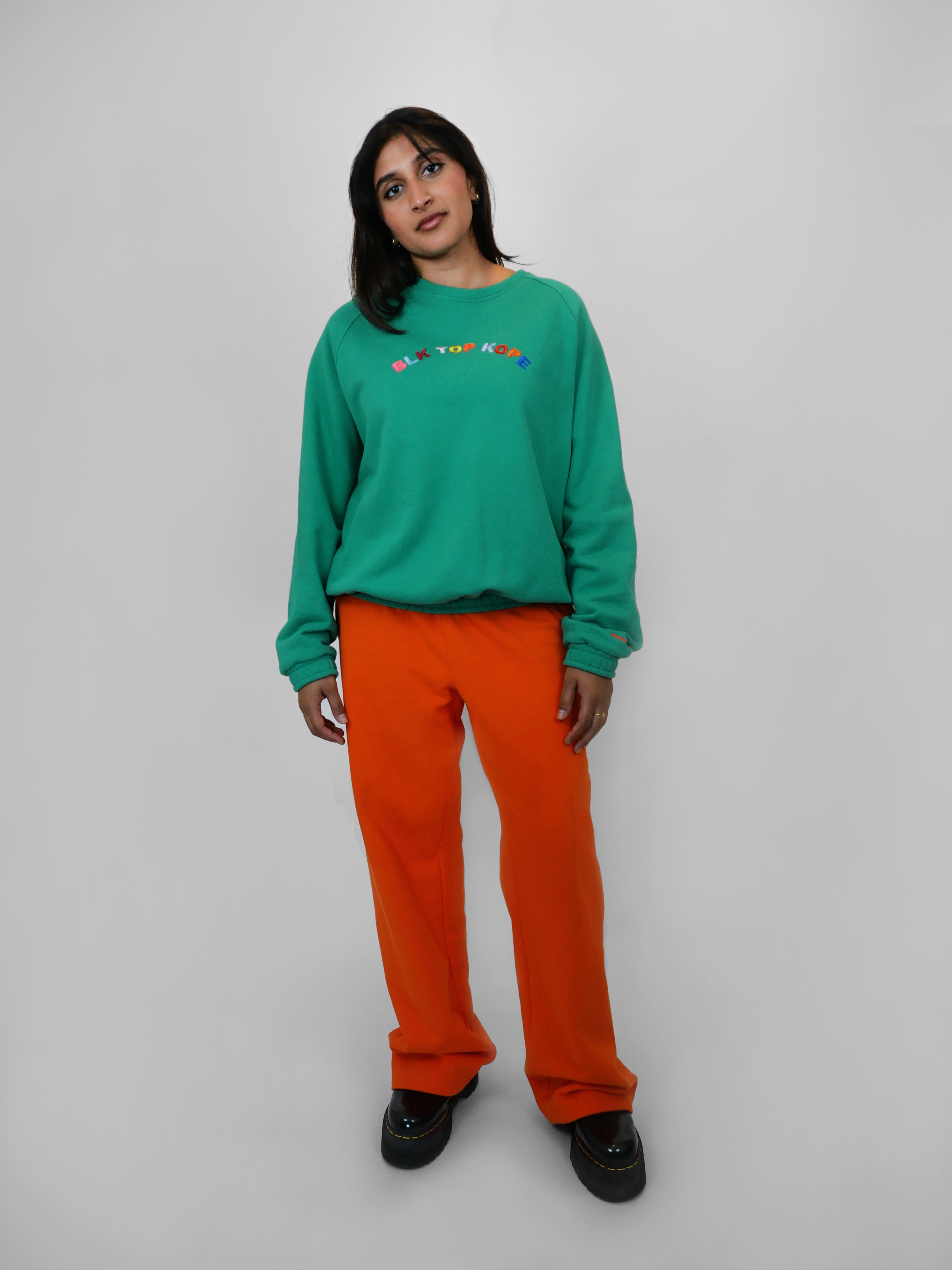 Person wearing a green sweatshirt and orange straight leg sweatpants on a white background