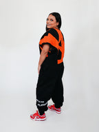 Person wearing an orange and black sweatervest with red sneakers on a white background