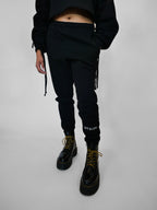Person wearing black sweatpants with brand logo and black boots on a light gray background