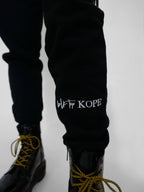 Black sweatpants with 'blk top Kope' branding worn by a person on a white background