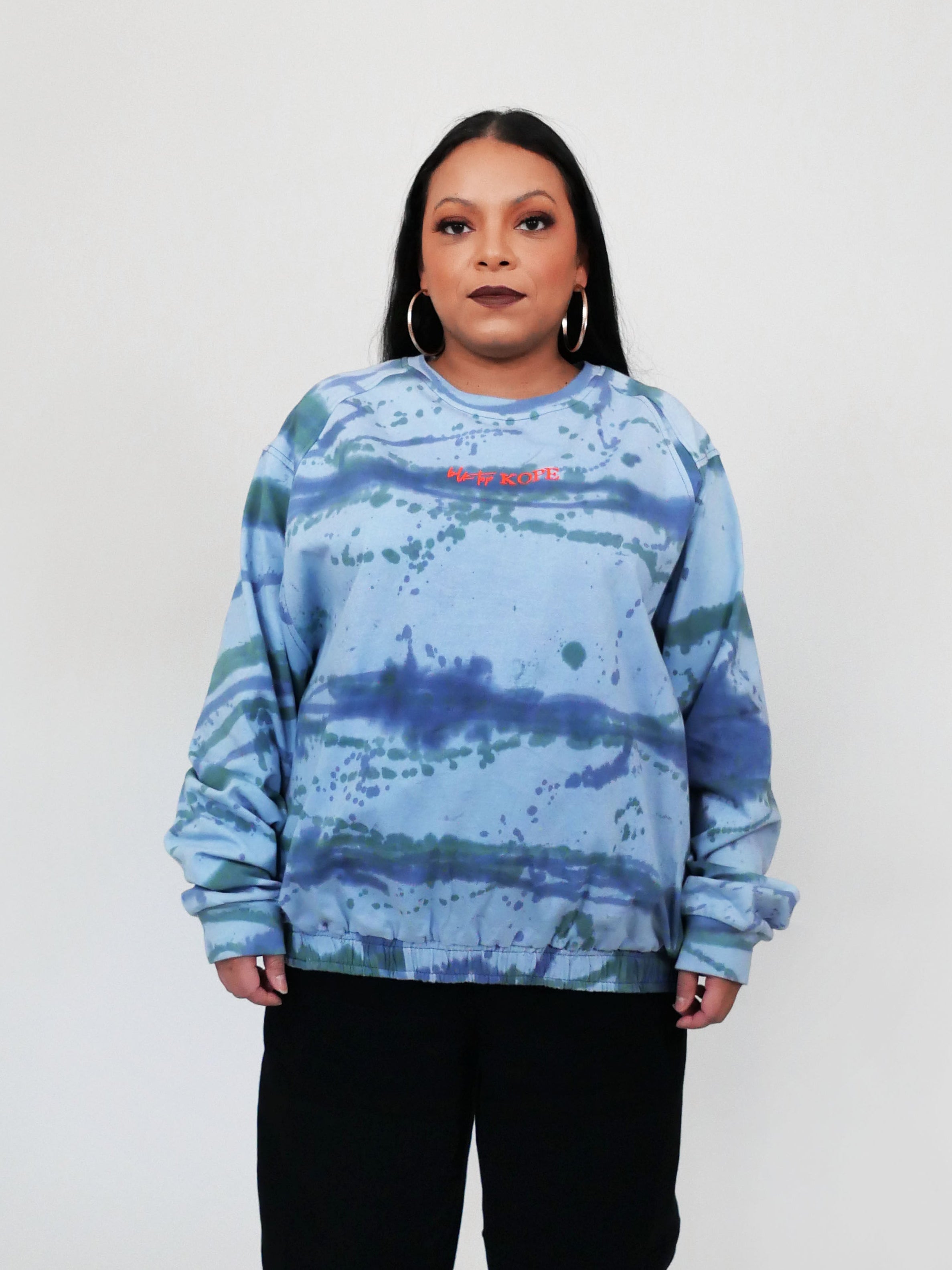 Person wearing a blue tie-dye longsleeve and black sweatpants with red shoes on a white background