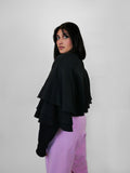 Woman wearing a black volant jacket and blush sweatpants against a white background