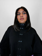 Person wearing a black volant jacket with snap buttons against a plain background