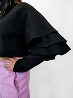 Black volant sleeve top worn by a person with a white background