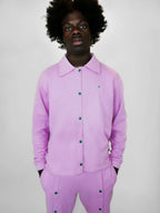 Person wearing a blush snap jacket with green snap buttons on a plain background