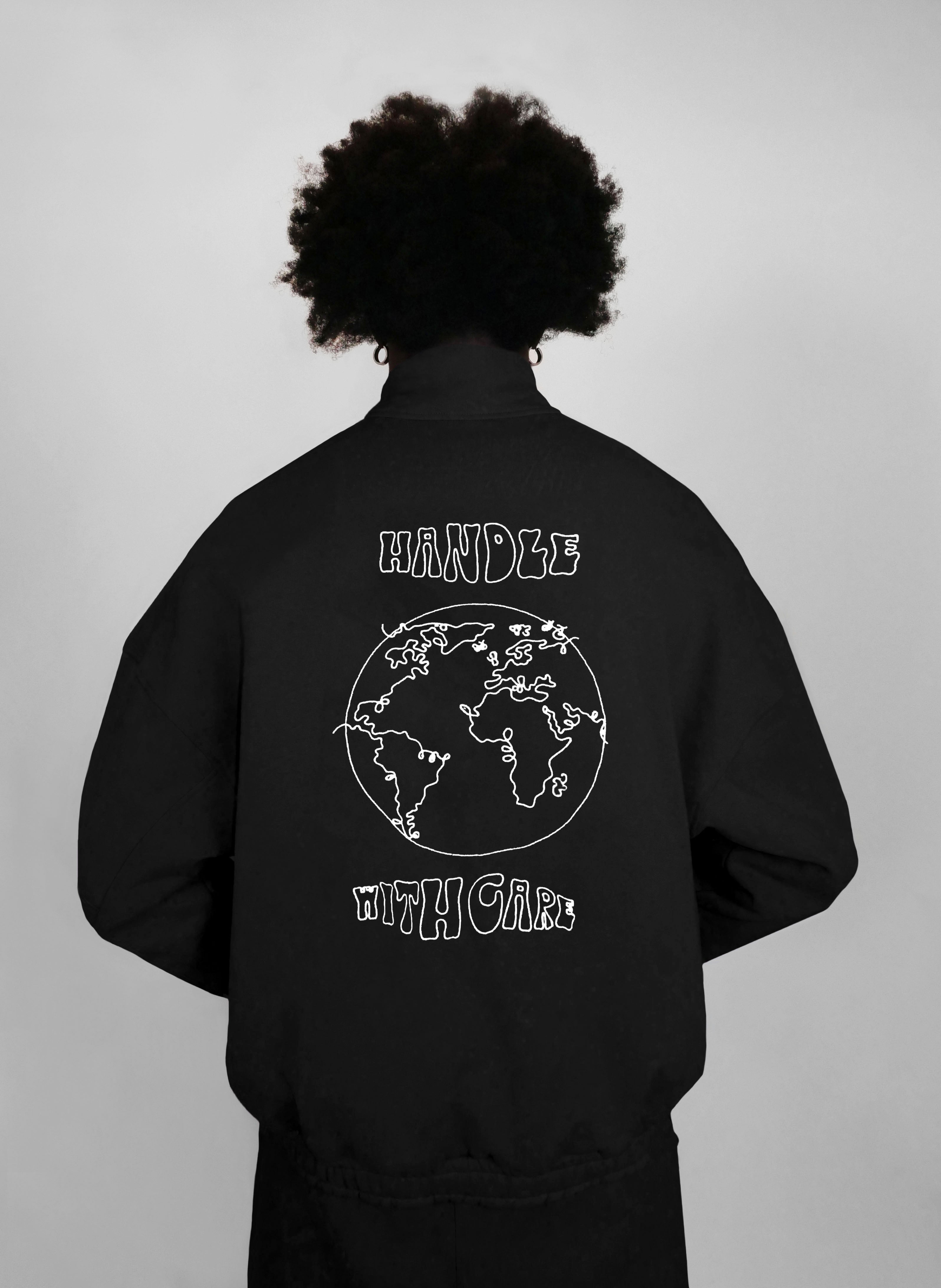 Person wearing a black zip-up with a world map design and text on the back, against a plain background.