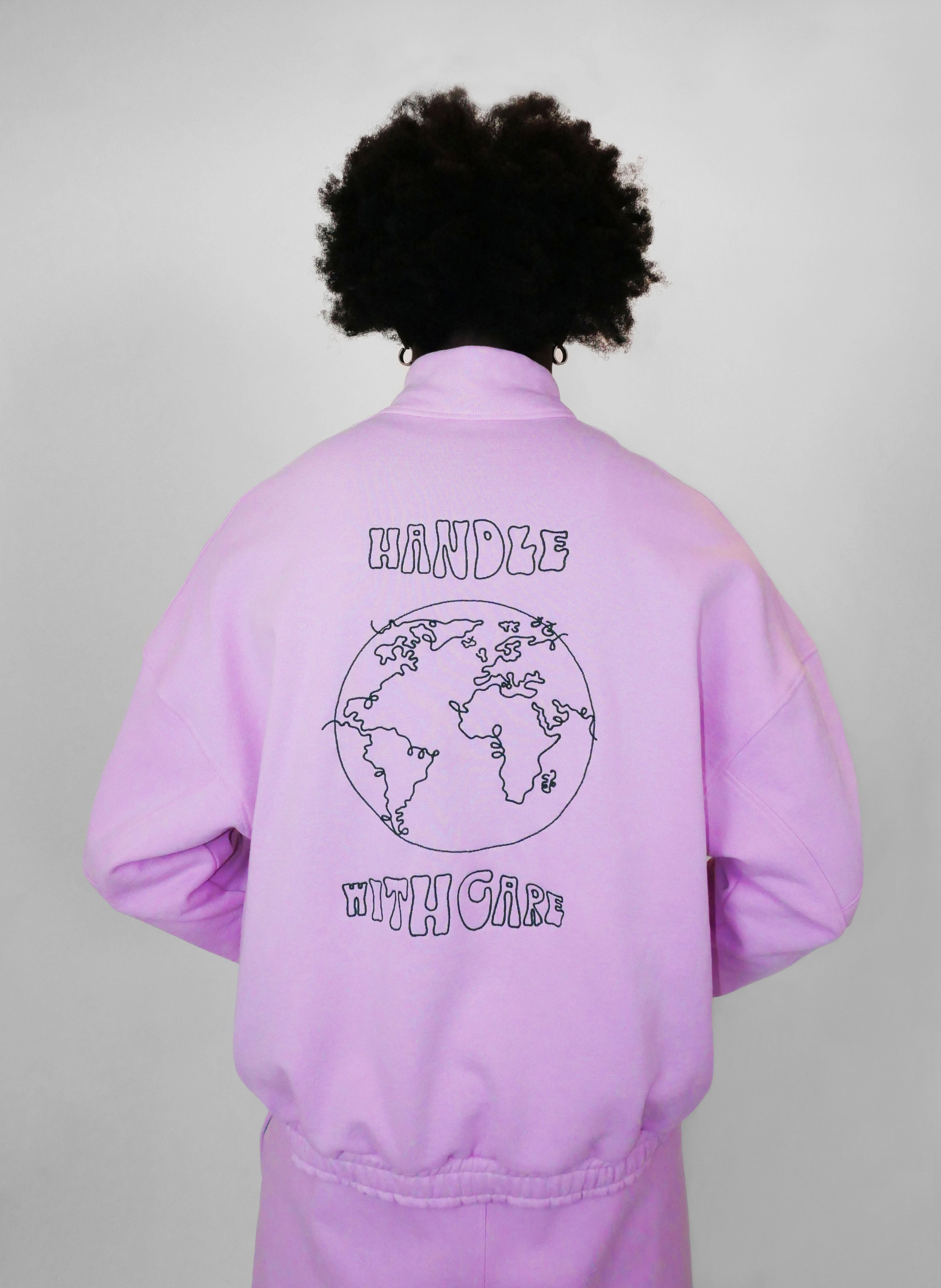 Person wearing a blush zip-up with a world map design on the back against a plain background