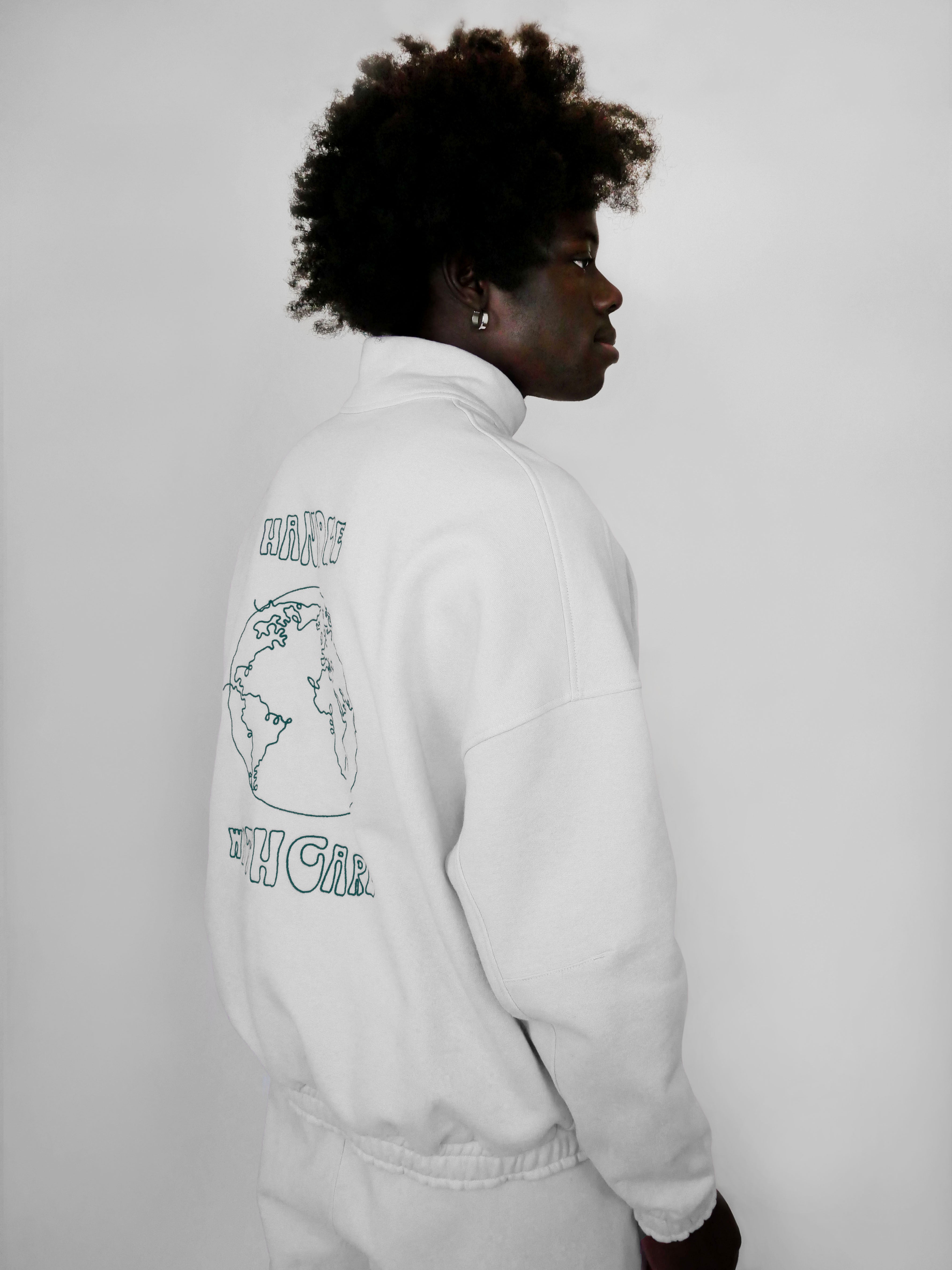 Person wearing a white zip-up with a world map design on the back against a plain background