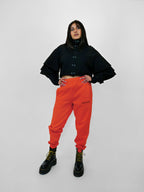 Person wearing a black volant snap jacket and orange sweatpants on a white background