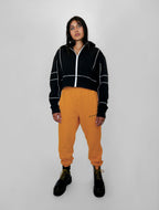 Person wearing a black jacket with white accents and yellow sweatpants on a white background