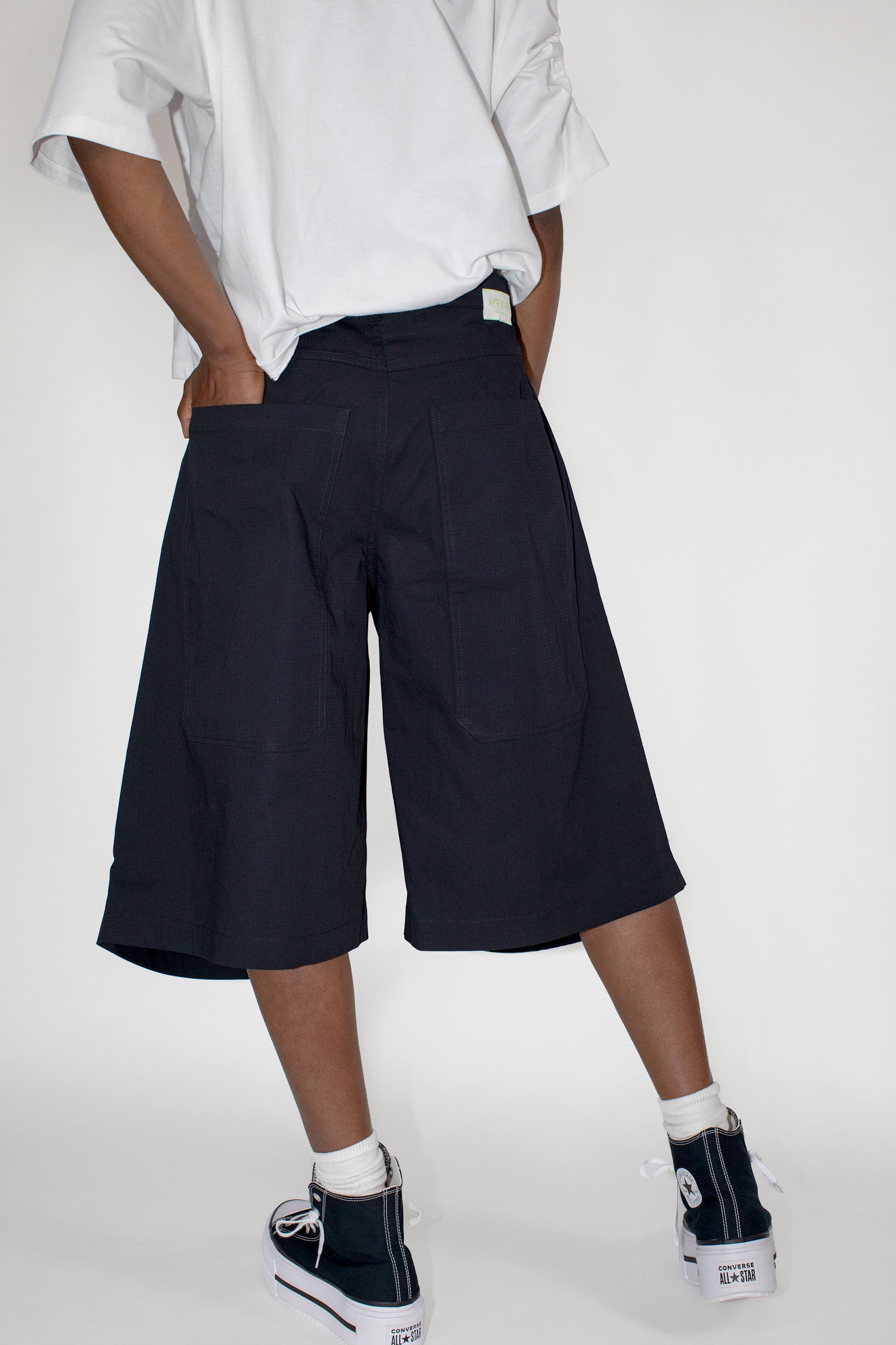 Person wearing black wide-leg shorts and white sneakers on a white background