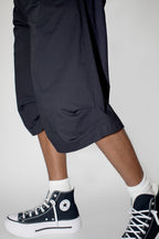 Person wearing black baggy shorts and black high-top sneakers with white laces on a plain background