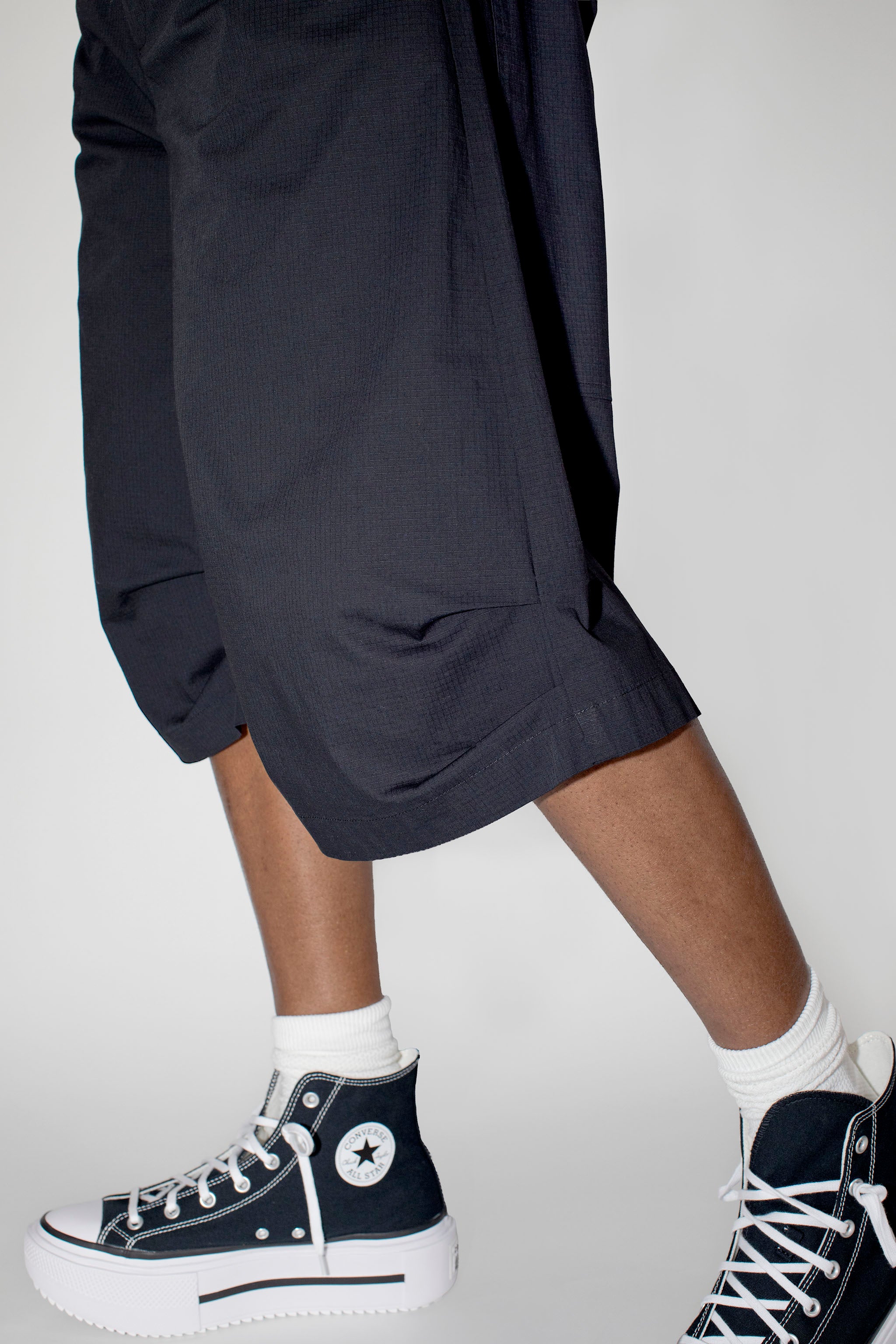 Person wearing black baggy shorts and black high-top sneakers with white laces on a plain background