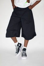 Person wearing black wide-leg shorts and black sneakers on a white background