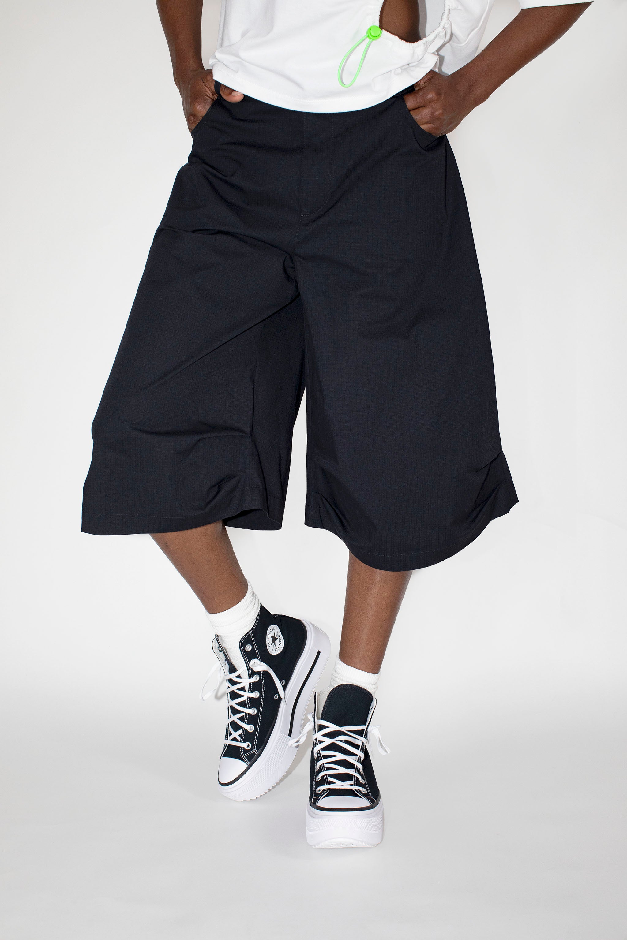 Person wearing black wide-leg shorts and black sneakers on a white background