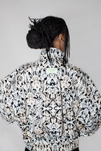 A person shown from the back wearing a high-neck, voluminous jacket with an all-over black and white abstract symmetrical pattern, set against a plain light gray background.