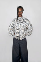 A model stands against a light gray studio background wearing a balloon track jacket with a black-and-white abstract pattern and dark wide-leg pants.