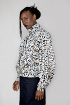 A model wearing a black and white abstract patterned high-neck track jacket with dark trousers, photographed against a solid light gray studio background.